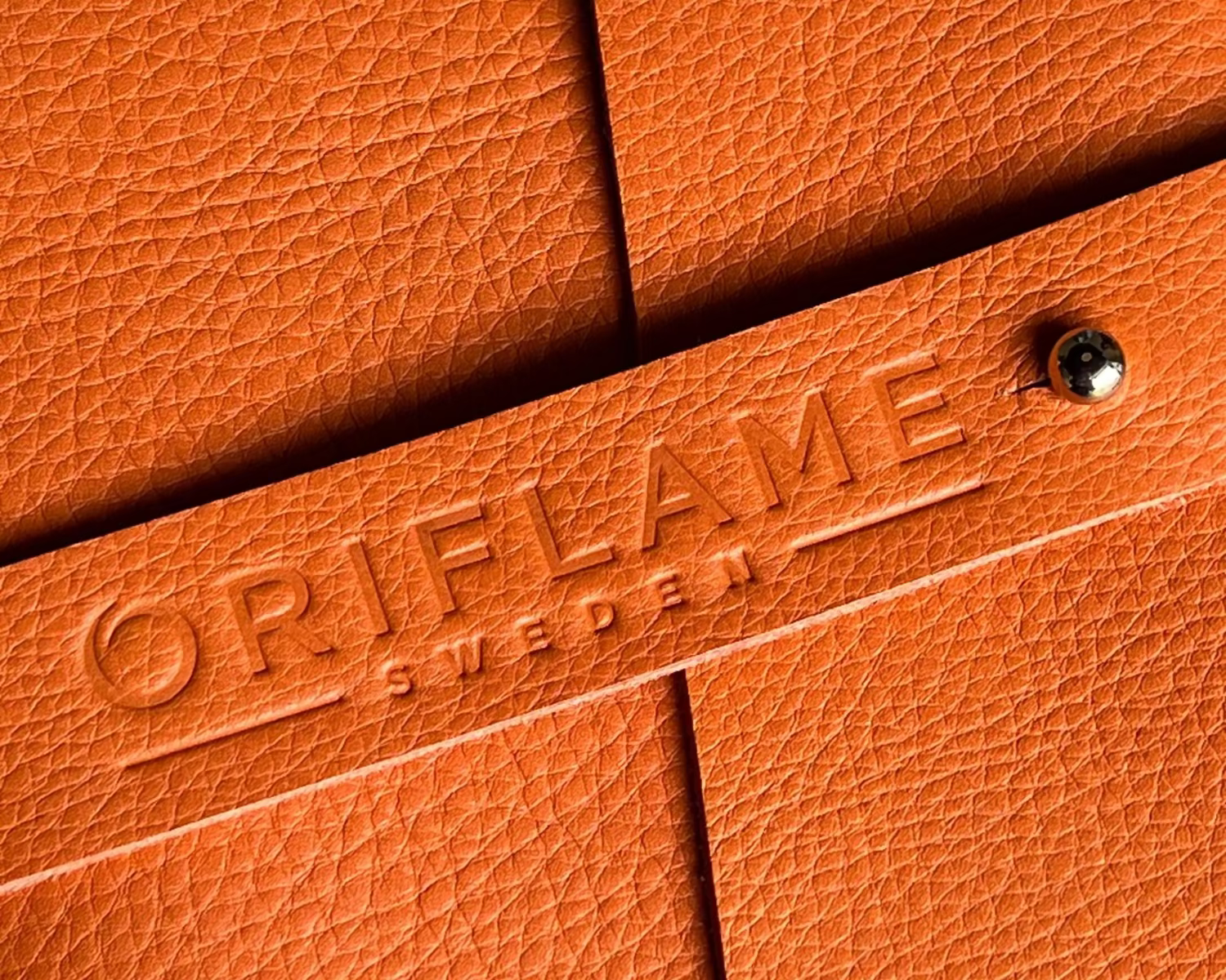 Close-up of orange leather notebook with 'ORIFLAME' branding.